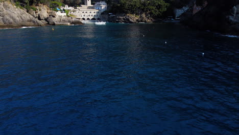 Drone-tilting-over-a-couple-on-a-yacht,-at-the-San-Fruttuoso-abbey,-in-sunny-Italy