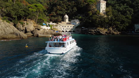 Drone-following-the-Gulfo-Paradiso-ferry,-landing-at-the-San-Fruttuoso-abbey,-Italy