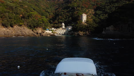 Drone-Volando-Sobre-Un-Barco-Que-Sale-De-La-Abadía-De-San-Fruttuoso,-En-La-Soleada-Italia