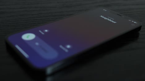 Close-up-shot-of-an-iPhone-receiving-a-call-from-a-neighbour-on-black-wooden-table