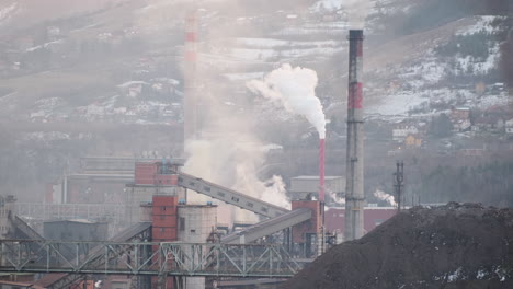 El-Vapor-Y-El-Humo-Se-Elevan-Desde-Un-Complejo-Industrial,-Con-Transportadores-Y-Un-Gran-Montículo-De-Carbón-En-Primer-Plano-Con-El-Telón-De-Fondo-De-Una-Ladera-Residencial-Nevada.