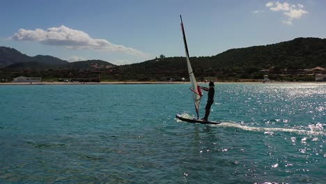 Windsurfers-lifting-his-thumb-for-the-camera-while-surfing-on-the-coast-of-Costa-Smeralda,-sunny,-summer-day-in-Sardinia,-Italy---Aerial-view