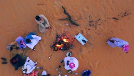 Aerial-view-of-people-gathered-around-a-bonfire-at-a-desert-camp,-sunset---top-down,-drone-shot