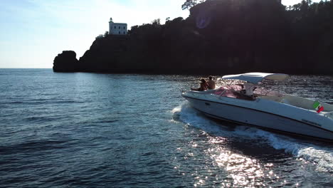 Boat-in-front-of-the-Portofino-lighthouse,-sunny-day-in-Italy---Aerial-view