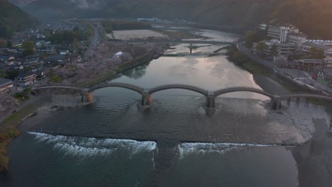 Alta-Vista-Aérea-Del-Amanecer-Sobre-La-Ciudad-De-Iwakuni-Y-El-Puente-Kintaikyo,-Japón