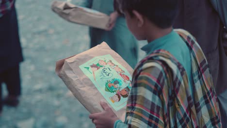 Rear-view-of-a-young-Pakistani-boy-holding-food-in-Iftar-drive-in-Balochistan,-Pakistan