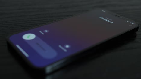 Close-up-shot-of-an-iPhone-receiving-a-call-from-Grandma-on-black-wooden-table