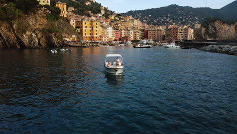 Aerial-view-flying-backwards-in-front-of-a-boat-leaving-Camogli,-golden-hour-in-Italy