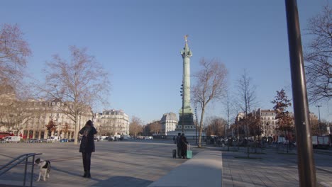 Persona-Y-Perro-Paseando-Por-La-Calle-Con-La-Columna-De-Julio-En-La-Place-De-La-Bastille-En-París,-Francia