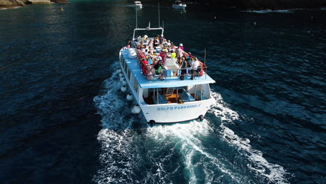 Aerial-tilt-shot-of-a-tourist-tour-ferry-closing-in-on-the-San-Fruttuoso-abbey,-in-Italy