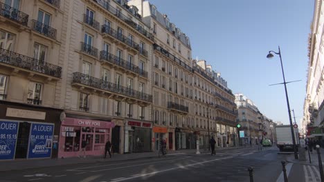 Taxi-Und-Leute,-Die-Mit-Dem-Motorroller-Entlang-Der-Pariser-Straße-Mit-Typischen-Gebäuden-Und-Geschäften-In-Paris,-Frankreich-Fahren