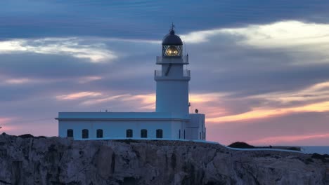 Aerial-panoramic-sunset-landscape-of-Cavalleria-lighthouse-Menorca-Cliff-ocean-golden-sky-with-pink-magenta-tones-flying-clouds-background-shot