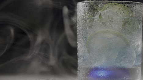 A-revolving-glass-filled-with-lemon-mint-drink,-enveloped-by-swirling-smoke,-embodies-the-concept-of-refreshment-and-relaxation