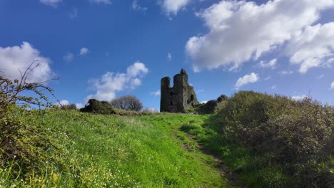 Ländlicher-Szenenpfad-Zur-Historischen-Mittelalterlichen-Burg-Dunhill-An-Einem-Wunderschönen-Frühlingstag-Mit-Blauem-Himmel-Und-Hellen-Wolken,-Die-An-Einer-Landschaftsszene-In-Waterford,-Irland-Vorbeiziehen