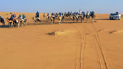 Aerial-view-around-nomads,-riding-camels-on-the-Arabian-desert,-during-golden-hour,-in-Saudi-Arabia---orbit,-drone-shot