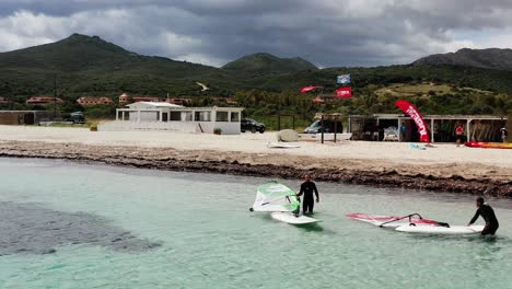 Luftaufnahme-Von-Menschen,-Die-An-Der-Costa-Smeralda,-Sardinien,-Auf-Ihre-Windsurfbretter-Steigen-–-Orbit,-Drohnenaufnahme