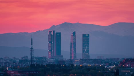 Zeitraffer-Der-Skyline-Von-Madrid-Mit-5-Türmen-Im-Geschäftsviertel-CTBA-Und-Schneebedeckten-Berggipfeln-Der-Sierra-Als-Hintergrund,-Sonnenuntergang,-Tag-zu-Nacht-Zeitraffer