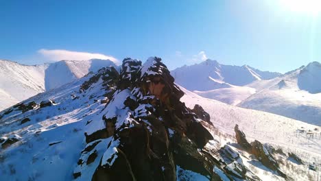 Beautiful-winter-rocks-against-the-backdrop-of-snow-capped-mountains-and-sunny-blue-skies-from-a-4k-drone