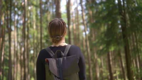 Young-Female-stands-admiring-tall-imposing-trees,-lush-forest-location