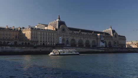Orsay-museum-building-and-tourist-boat-sail-nearby,-static-view