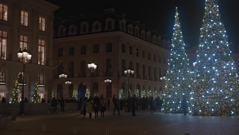 People-walk-by-Christmas-trees-and-buildings-at-night-in-Paris,-slomo