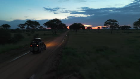 Drone-passing-a-offroad-vehicle,-driving-across-on-a-dirt-road,-sunset-in-Africa