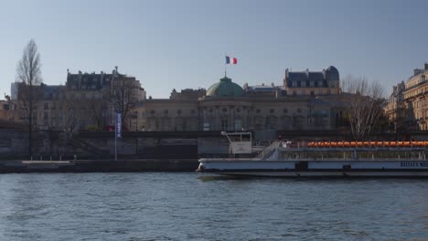 Bateau-Mouche-Pasando,-Edificio-Con-Bandera-Francesa-En-Segundo-Plano