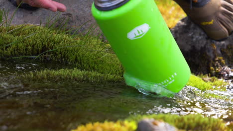 Man-filling-his-bottle-in-a-fresh-water-stream,-in-wilderness-of-Iceland---Slow-motion