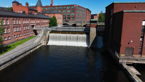 Drone-rising-away-from-Tammerkoski-power-plant,-sunny-day-in-Tampere,-Finland