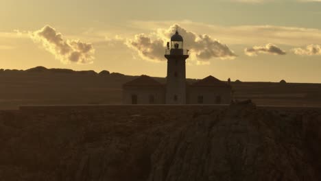 Sonnenuntergang-Skyline-Leuchtturm-über-Mediterraner-Klippenlandschaft-Luftdrohne-Punta-Nati-Menorca-Spanien-Orbit,-Goldener-Hintergrund