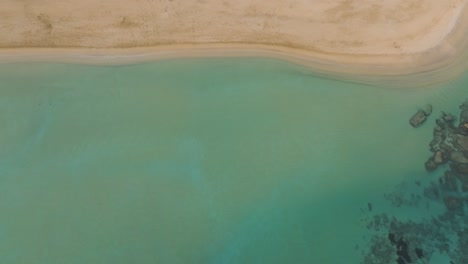 White-sand-beach-aerial-top-down-turquoise-sea-water-along-coastline-panning-islets-in-pale-tones