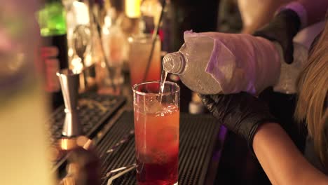 Bartender-prepares-tequila-sunrise-cocktail-by-pouring-water-into-glass