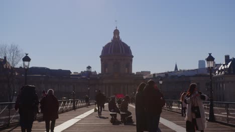 People-Walking-In-Pont-des-Arts-With-Institut-de-France-Building-In-Paris,-France