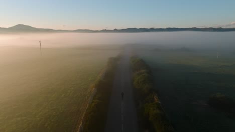 Road-between-foggy-mountain-valley-with-a-person-morning-jogging-aerial-drone-panoramic-view
