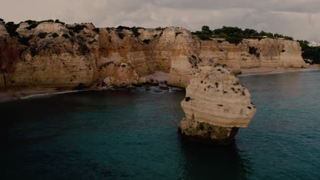 Drone-flying-through-rocky-Algarve-Coastline-in-Portugal-and-waves-crashing-in-on-the-beach-during-midday