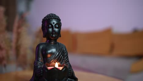 Langsam-Bewegte-Nahaufnahme-Einer-Buddha-Statue-Mit-Einer-Kerze-In-Gemütlicher-Wohnzimmeratmosphäre