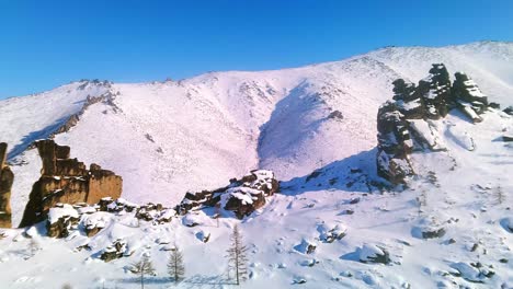 Hermoso-Vuelo-En-Un-Dron-Cerca-De-Rocas-Invernales-Con-El-Telón-De-Fondo-De-Montañas-Cubiertas-De-Nieve-Y-Un-Cielo-Azul-Soleado-4k