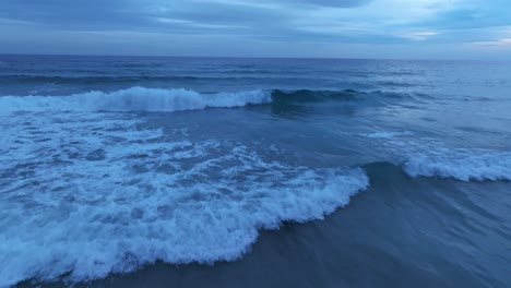 Blue-landscape-of-drone-flying-low-above-stormy-waves-aerial-breaking-above