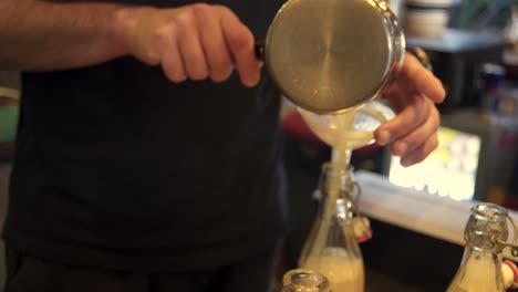 Side-view-of-bartender-pouring-lemon-juice-in-a-bottle-through-a-plastic-funnel