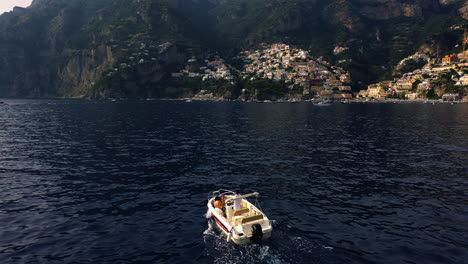 Drone-shot-following-a-boat-moving-toward-the-Positano-village,-golden-hour-in-Amalfi,-Italy