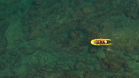 Aerial,-top-down,-drone-shot,-above-a-father-and-kid-rowing-on-a-row-boat,-in-shallow,-turquoise-water,-on-a-sunny-day,-on-the-coast-of-Istria,-Croatia