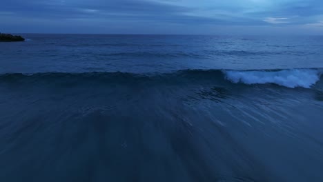 Closeup-to-beach-waves-breaking-after-sunset,-dusk-skyline-aerial-drone-closeup