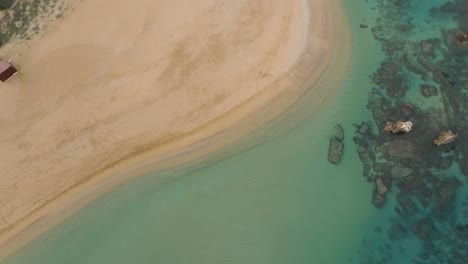 Aerial-Drone-Fly-Zooming-out-white-sand-beach-rocky-shore-forested-coastline-blue-sea-water,-going-up-tropical-paradise