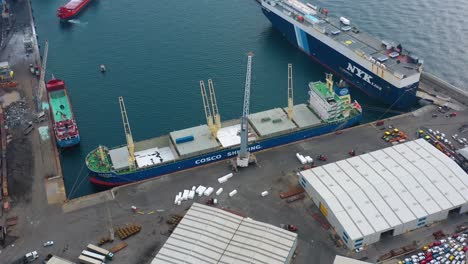 Aerial-drone-view-of-bulk-carrier-docked-at-a-marina,-in-cloudy-Savona-city,-Italy