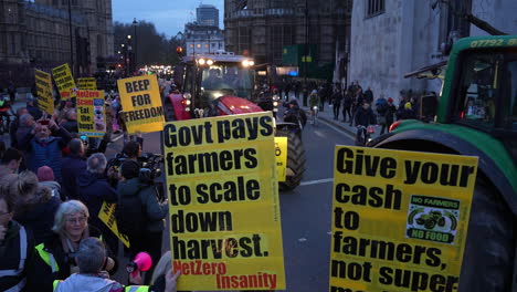 Protestors-hold-up-placards-that-read,-“Government-pays-farmers-to-scale-down-harvest”-and,-“give-your-cash-to-farmers-not-supermarkets”-as-a-convoy-of-tractors-pass-the-Houses-of-Parliament-at-dusk