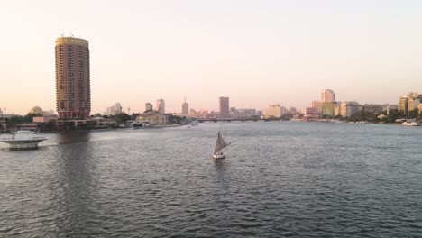 Aerial-over-river-Nile,-a-sailboat-on-the-water-with-the-Cairo-Tower-and-Sofitel-Cairo-Nile-El-Gezirah-hotel-in-the-background,-in-Cairo,-Egypt