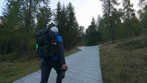 Hombre-Caminando-Por-El-Camino-En-El-Bosque-Con-Mochila-Sosteniendo-La-Cámara-En-La-Región-De-Valmalenco,-Italia