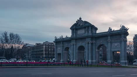 Zoom-In-Timelapse-shot-of-Puerta-de-Alcala-during-sunset-with-cars-and-traffic-as-foreground-cloudy-sunset-sky