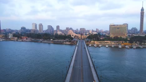 Vista-Aérea-De-Un-Puente-Que-Cruza-El-Río-Nilo-En-El-Centro-De-El-Cairo,-Egipto,-Con-La-Prominente-Estatua-De-Pacha-A-La-Vista,-Que-Ilustra-El-Concepto-De-Conectividad-Urbana-Y-Prominencia-Histórica.