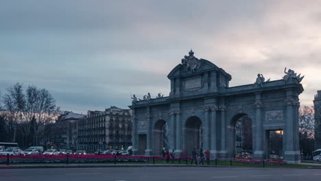 Detaillierte-Nahaufnahme-Im-Zeitraffer-Der-Puerta-De-Alcala-Bei-Sonnenuntergang-Mit-Autos-Und-Verkehr-Im-Vordergrund,-Wolkiger-Sonnenuntergangshimmel